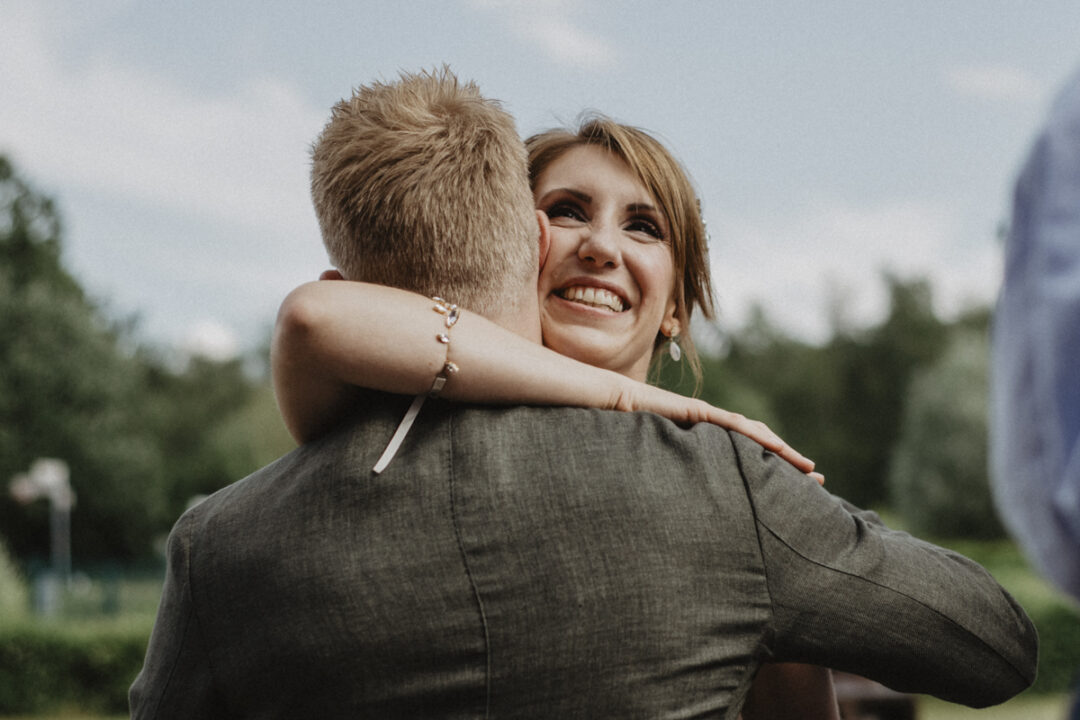 Braut umarmt lachend einen Gast nach der Trauung in Waltrop