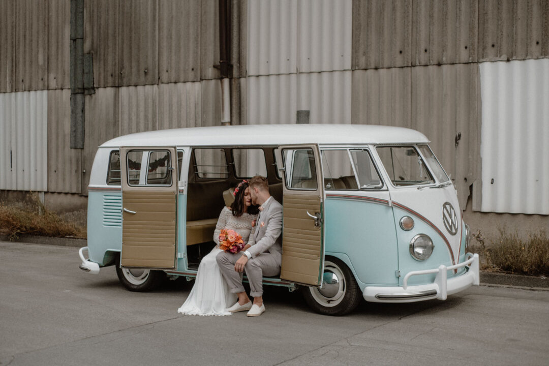 Paar sitzt im Bulli vor alter Halle