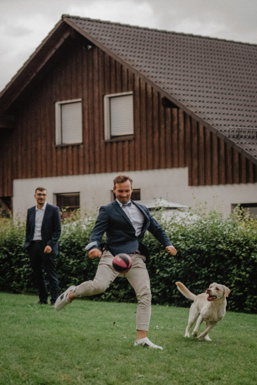 Hochzeitsgast spielt Ball mit Hund auf Wiese