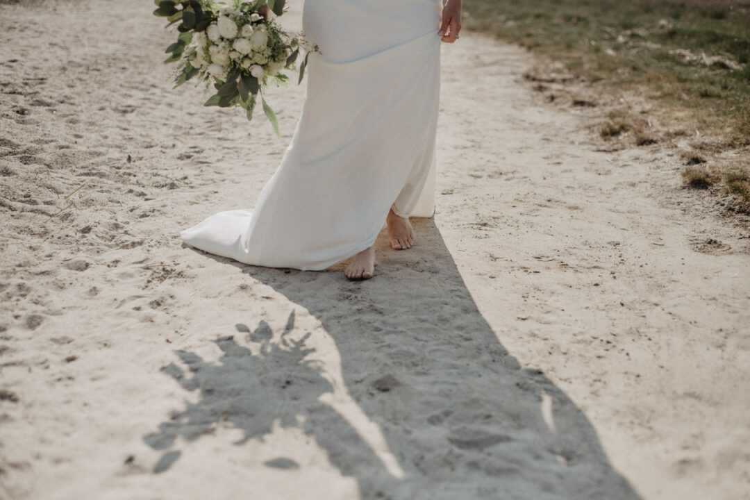 Braut läuft durch den Sand, nur Füße sichtbar