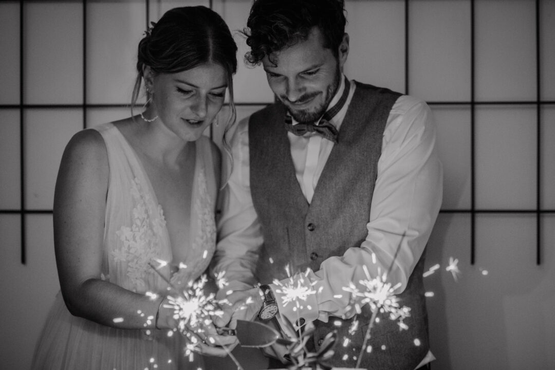 Brautpaar schneidet Hochzeitstorte mit brennenden Wunderkerzen an