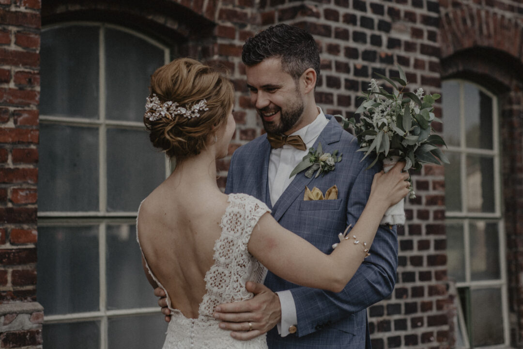 Brautpaar umarmt sich liebevoll vor Backsteinfassade in Waltrop