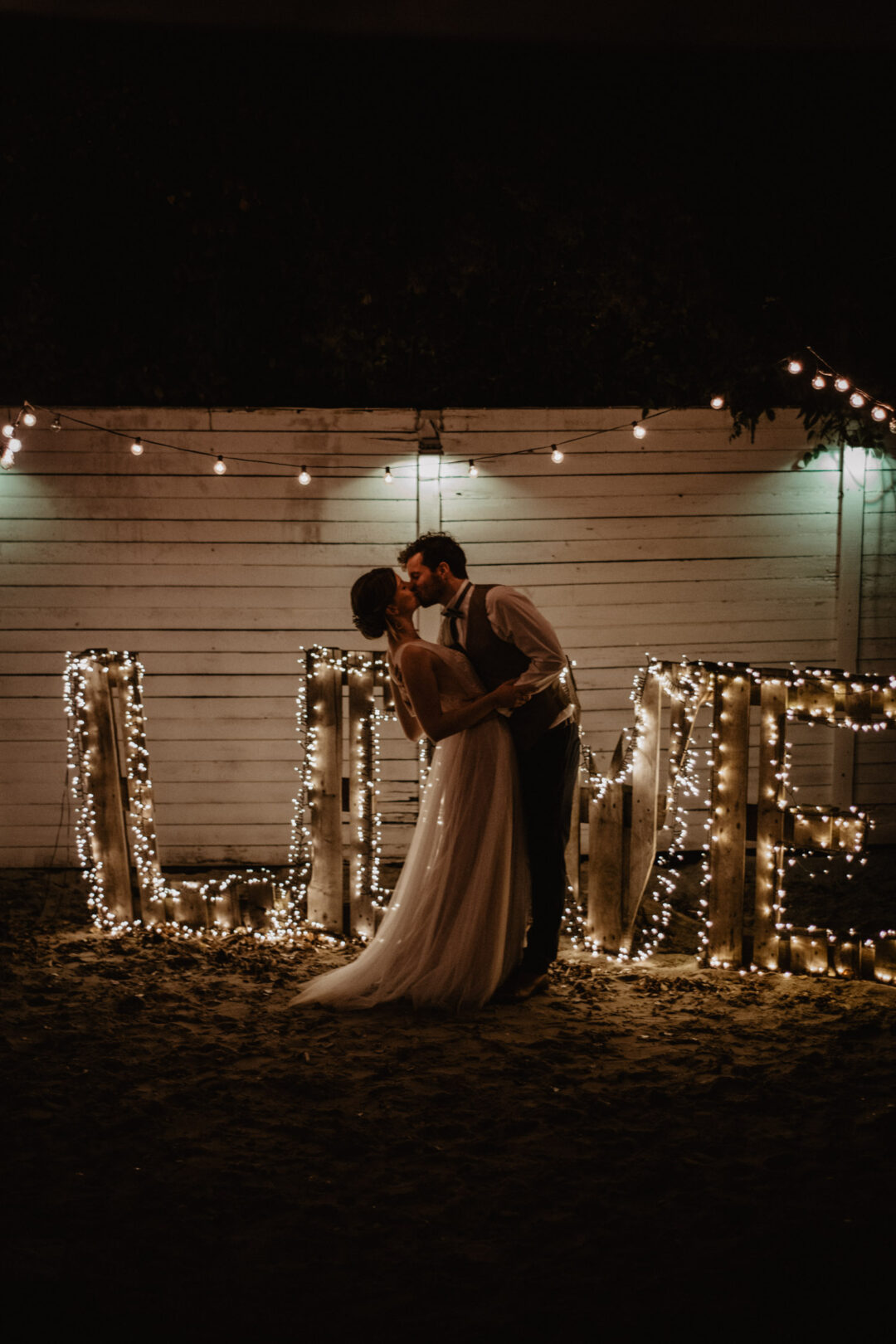 Kuss des Brautpaares unter romantischen Lichterketten