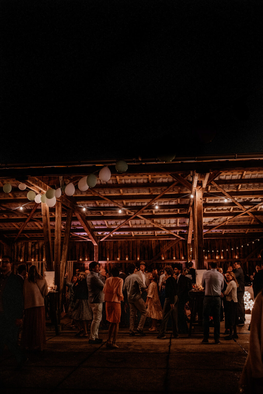 Scheunenhochzeit bei Nacht mit vielen Gästen und Lichterketten