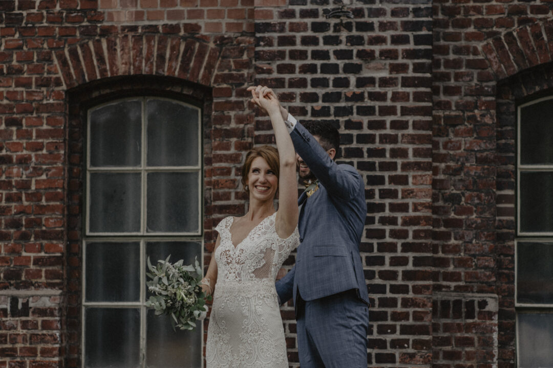 Brautpaar tanzt lachend vor Fabrikfenster