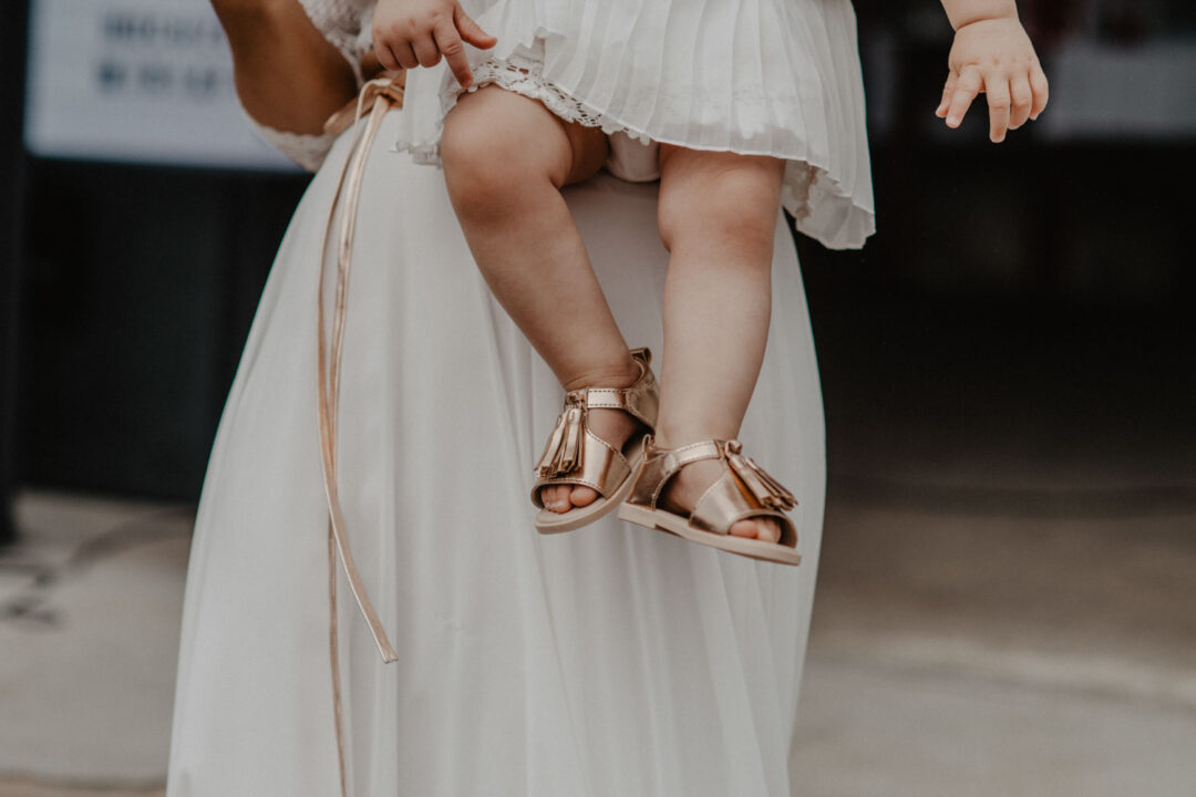 Kinderschuhe auf Brautkleid, goldene Sandalen