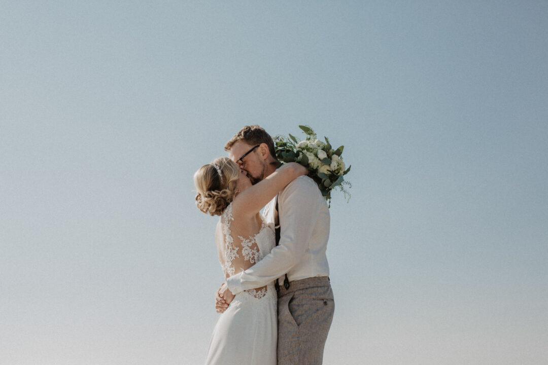 Bräutigam hebt die Braut und umarmt sie mit dem Brautstrauß