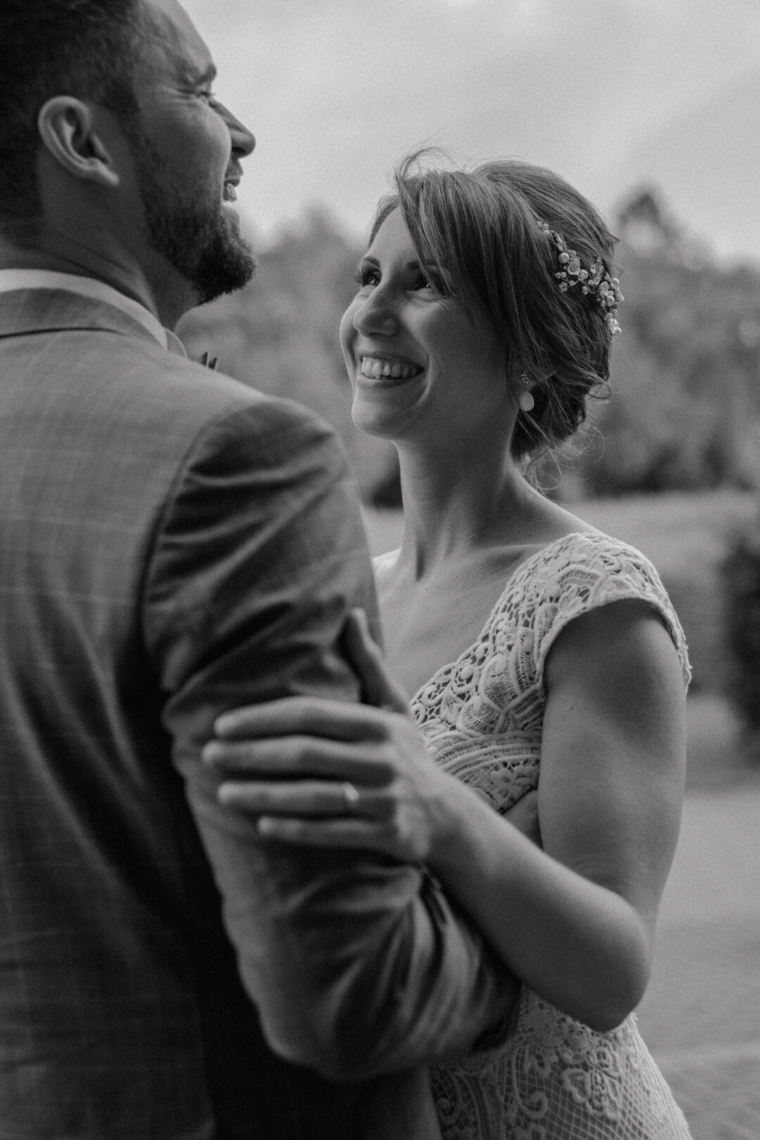 Schwarzweißaufnahme eines lachenden Brautpaares vor Backsteinwand