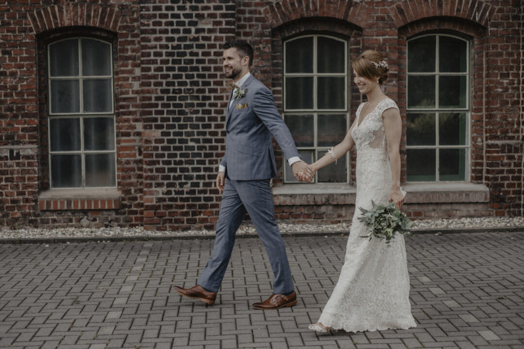 Brautpaar spaziert Hand in Hand entlang Backsteinfassade