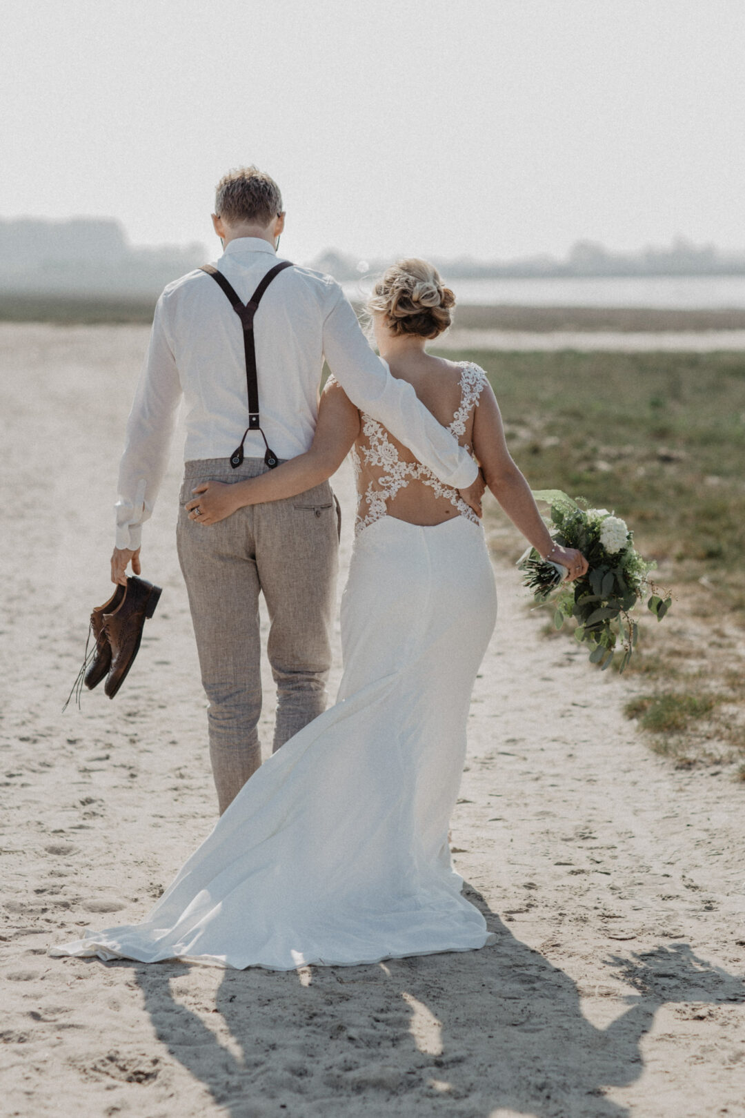 Braut und Bräutigam gehen Hand in Hand Richtung Wasser