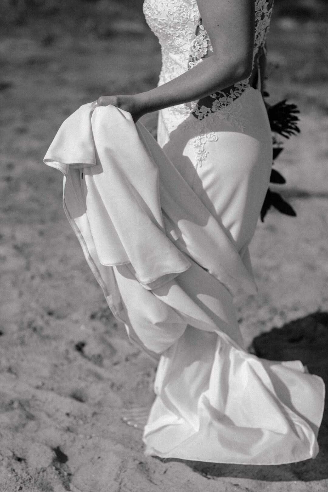 Braut hält ihr Kleid beim Gehen hoch, Schatten fällt auf den Sand