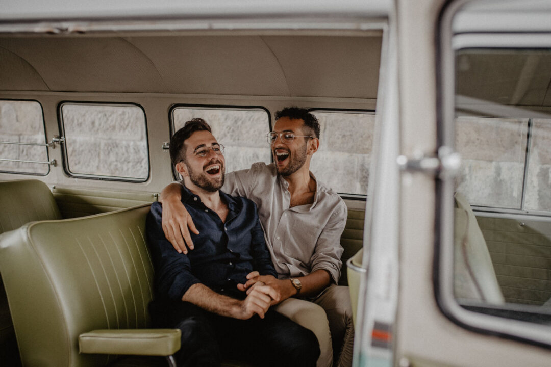 Zwei Männer lachen verliebt im VW Bus