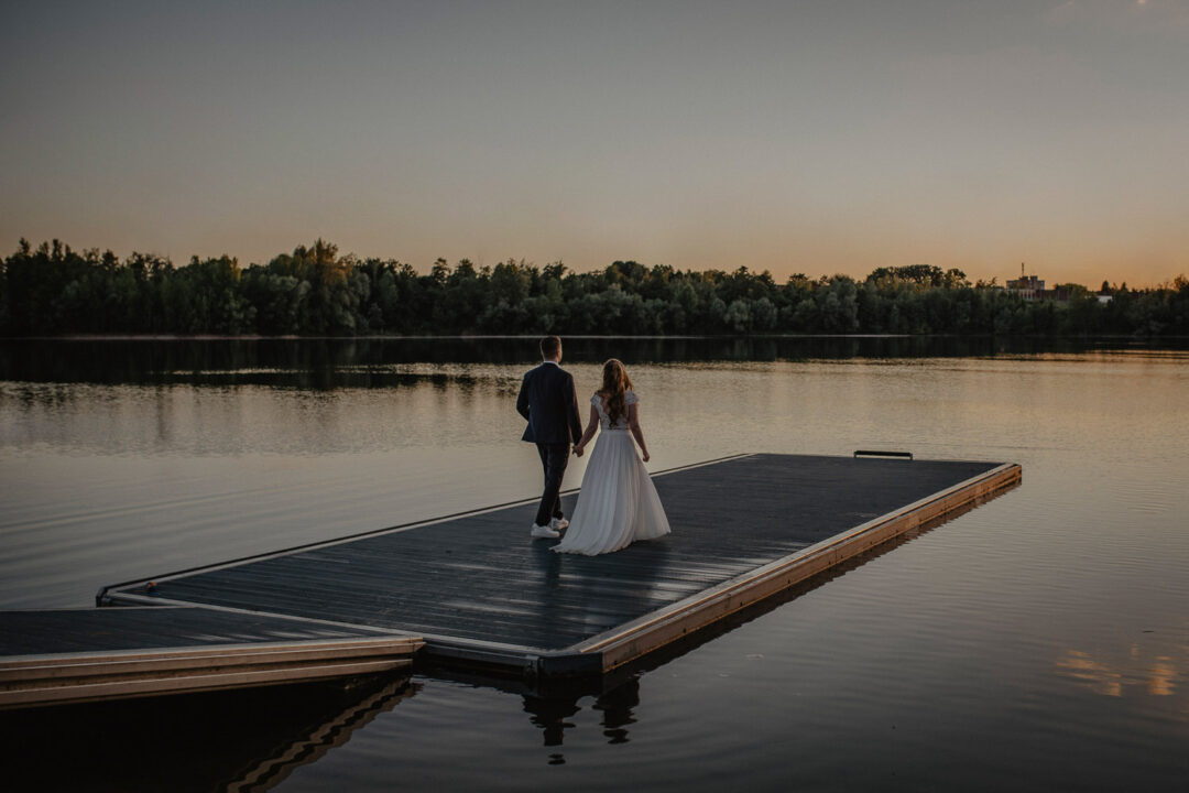 Brautpaar läuft Hand in Hand am Steg