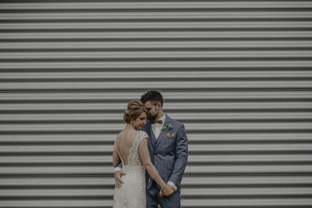 Brautpaar vor industrieller Wand in romantischer Pose