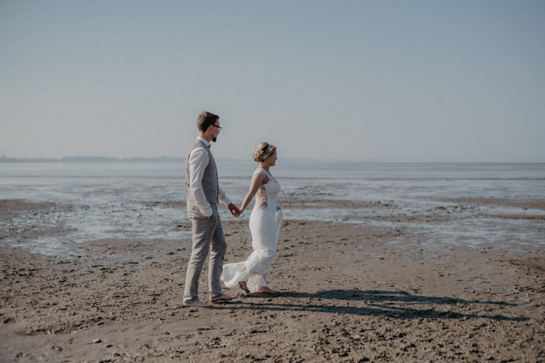 Braut und Bräutigam halten sich an der Hand und gehen am Ufer