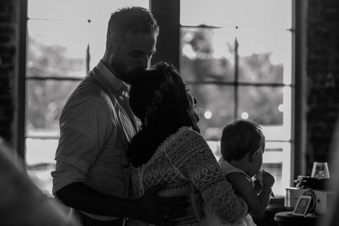 Bräutigam küsst Braut auf den Kopf, Kind im Arm