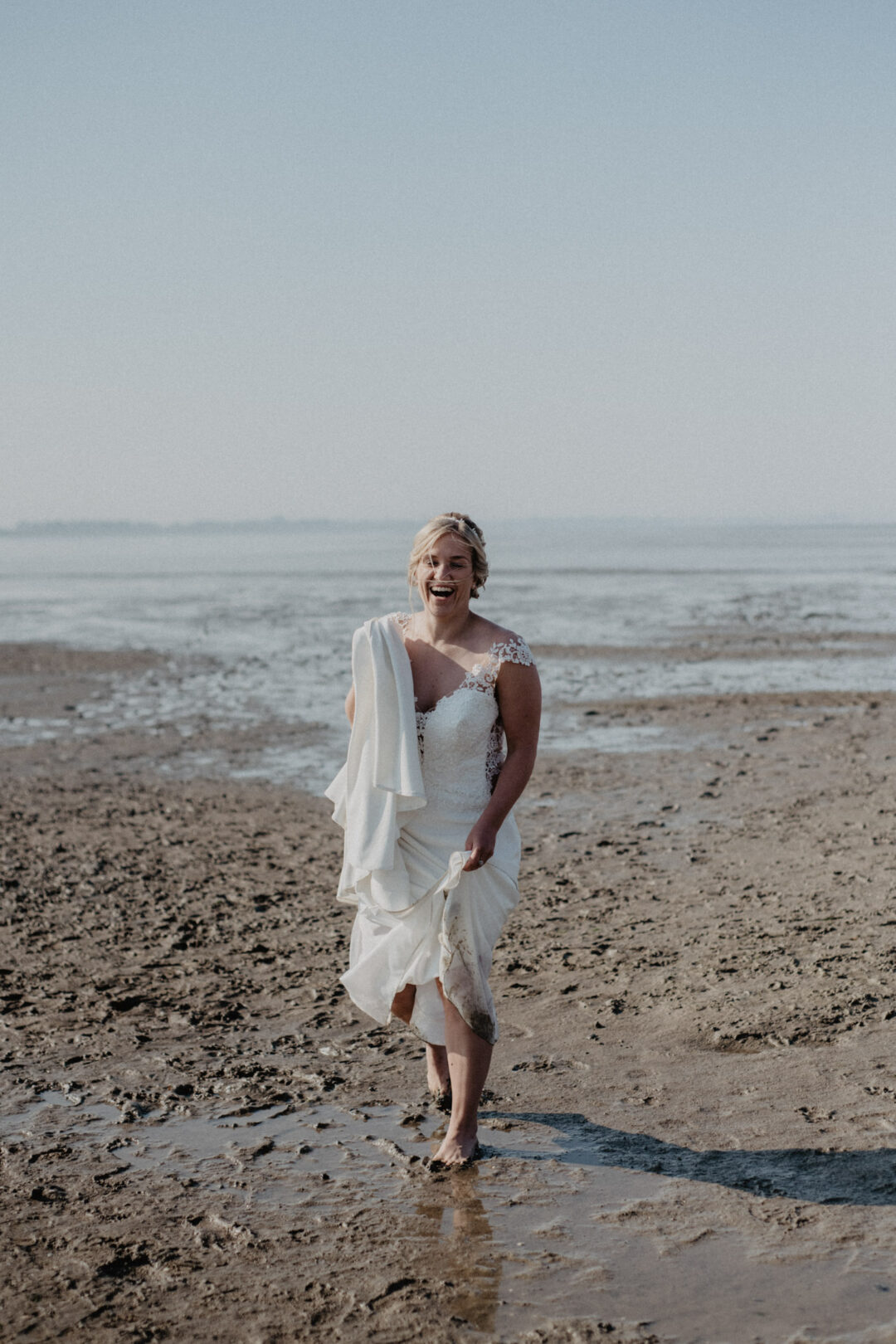 Braut steht allein im Sand mit Blick zur Kamera