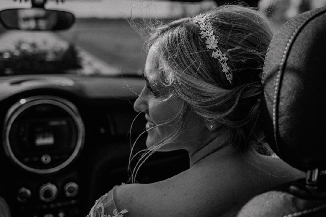 Braut sitzt lächelnd im Auto – Schwarz-Weiß