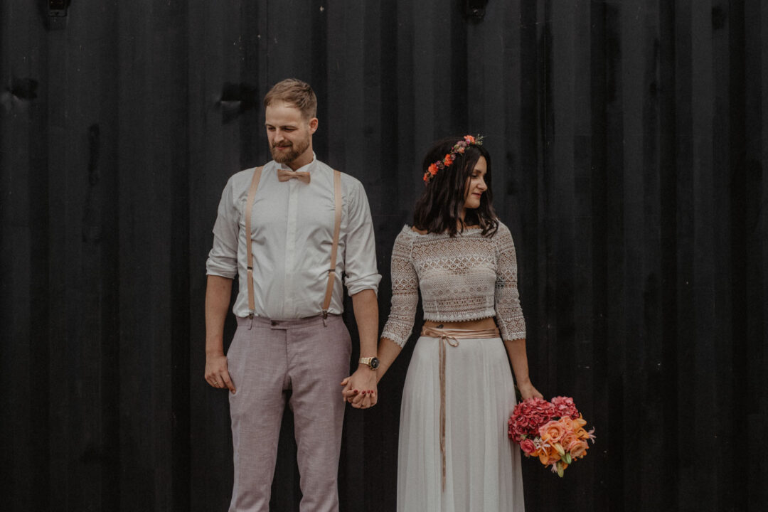 Brautpaar hält sich an schwarzer Wand an der Hand