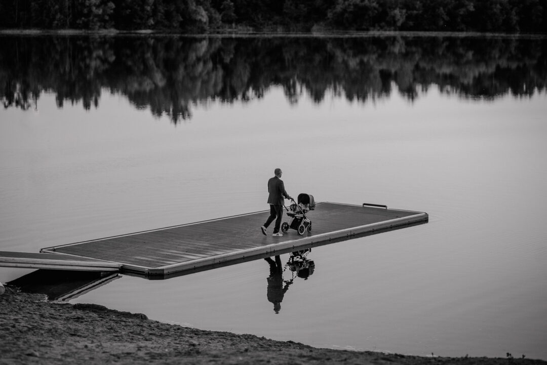 Vater schiebt Kinderwagen am Wasser