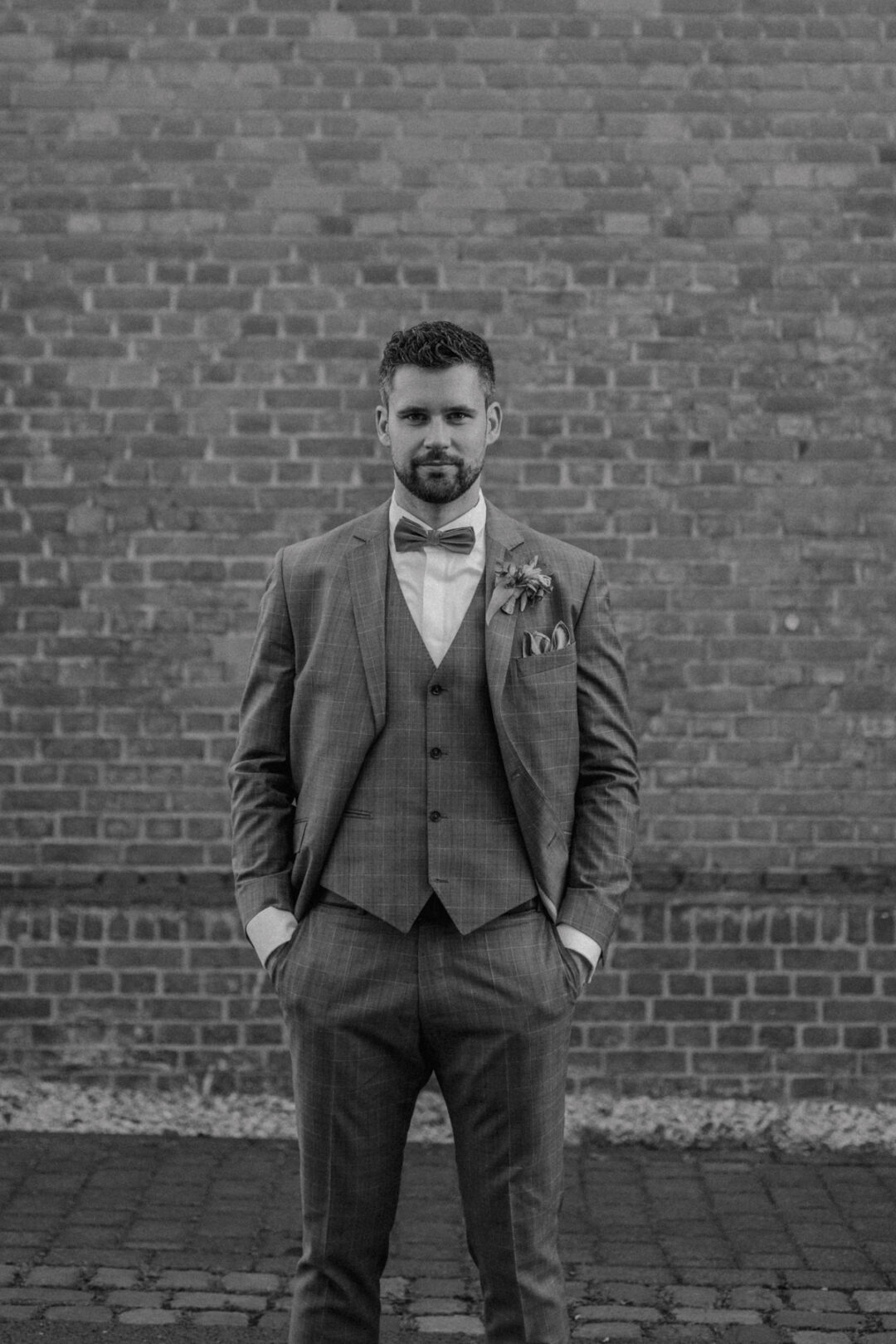 Bräutigam steht vor Backsteinwand in Schwarz-Weiß