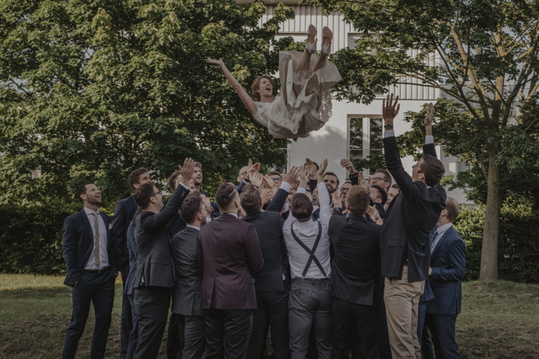 Hochzeitsgäste werfen die Braut lachend in die Luft