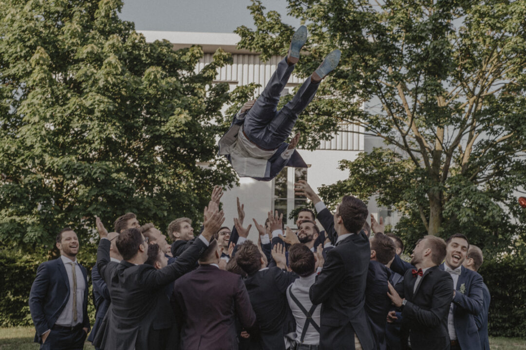 Bräutigam wird von Hochzeitsgästen in die Luft geworfen