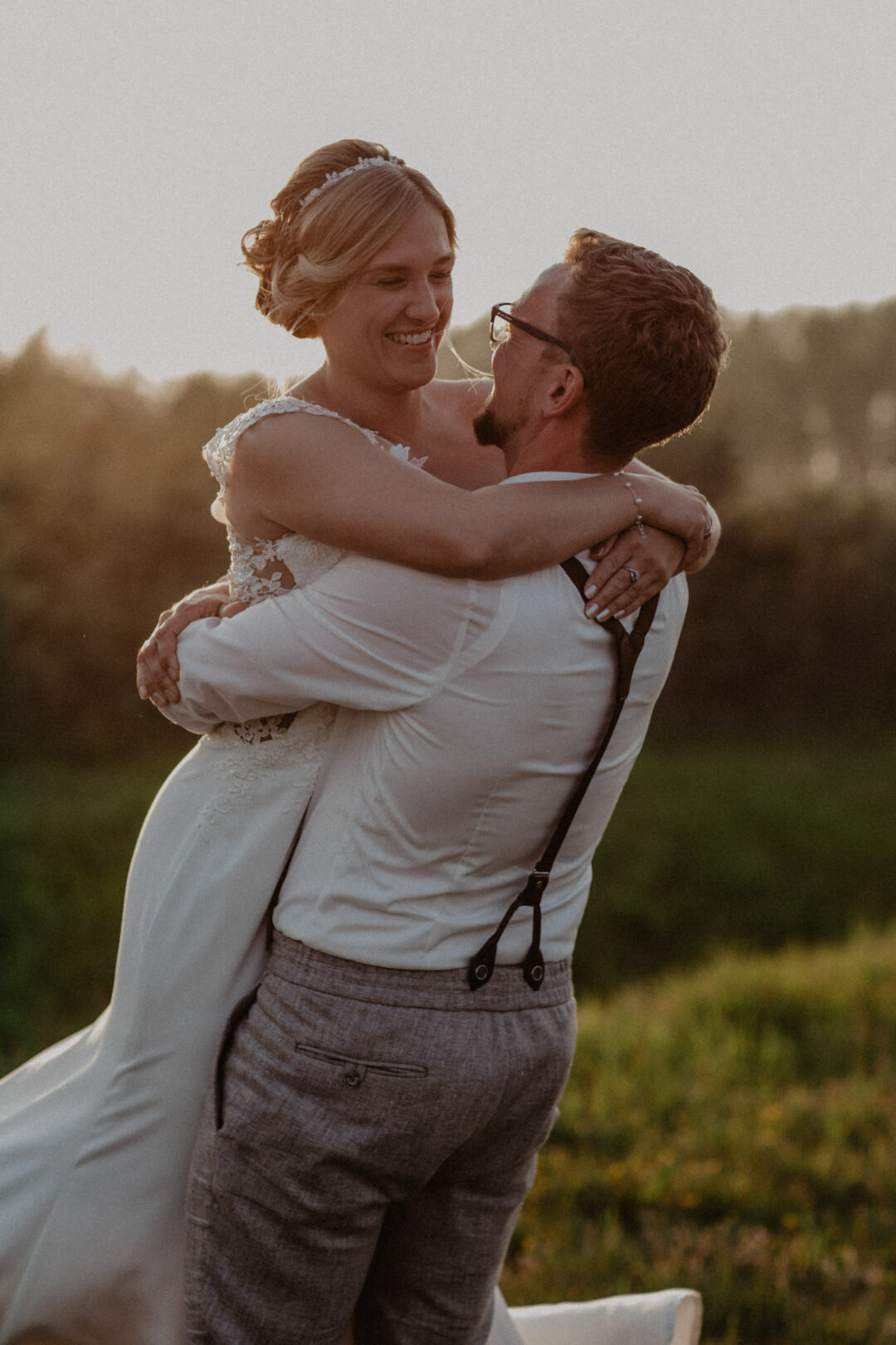 Bräutigam hebt die Braut im Sonnenuntergang hoch