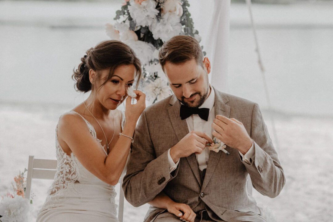 Braut wischt Tränen, Bräutigam richtet Anstecker bei Trauung