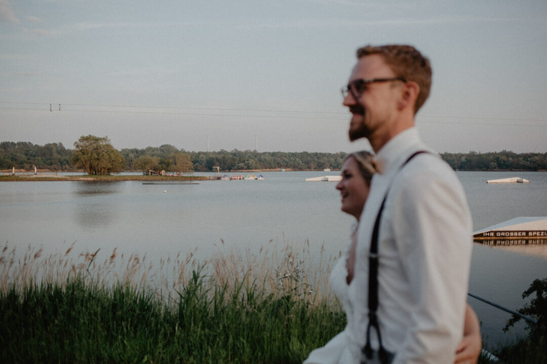 Bräutigam blickt über das Wasser bei Sonnenuntergang