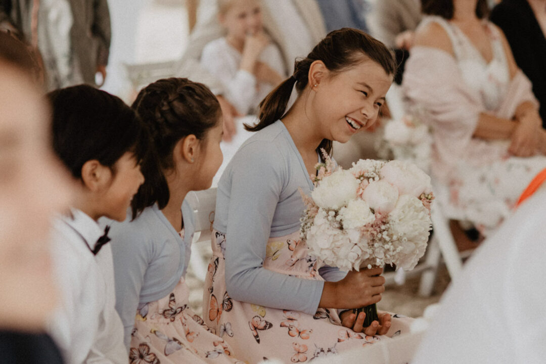 Mädchen mit Brautstrauß lacht während Strandhochzeit