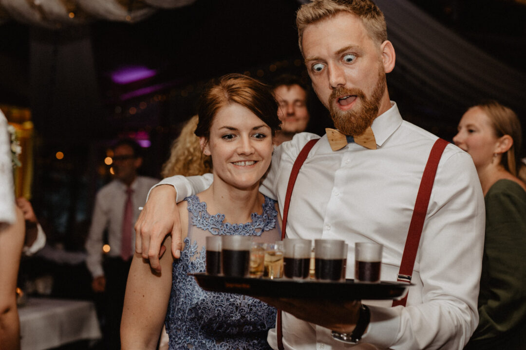 Trauzeuge bringt Tablett mit Drinks, Gäste lachen