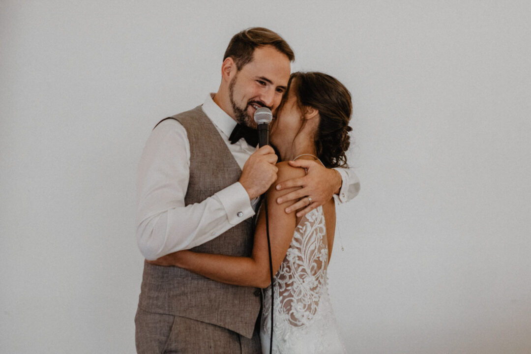 Bräutigam hält Rede mit Braut am See im Arm