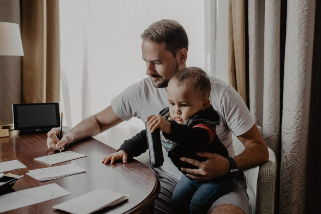 Bräutigam schreibt mit Kind auf dem Schoß im Hotelzimmer