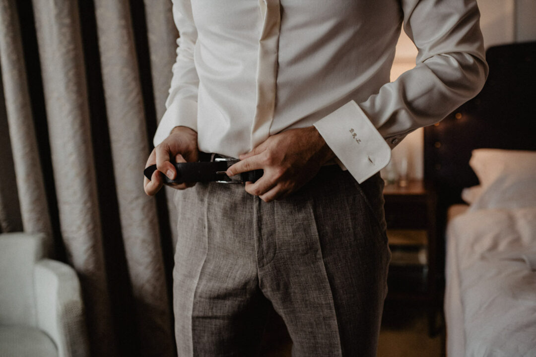 Bräutigam legt Gürtel beim Anziehen im Hotelzimmer an