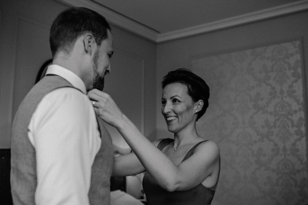 Frau richtet dem Bräutigam die Krawatte in Schwarz-Weiß