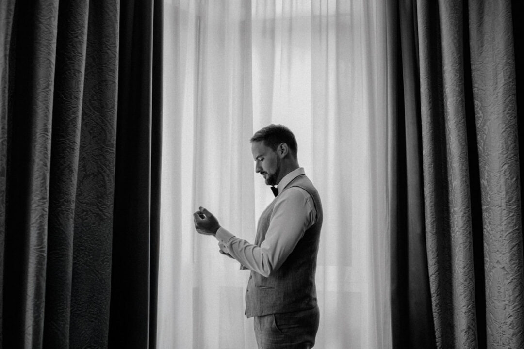 Bräutigam richtet Ärmel allein am Fenster, schwarzweiß