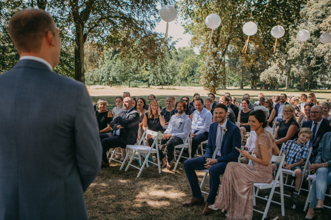 Gäste sitzen lachend bei der Trauung im Freien