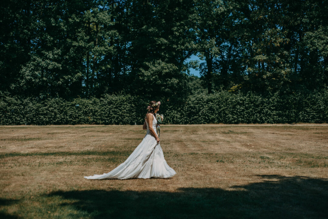 Braut geht allein über Wiese zur Trauung