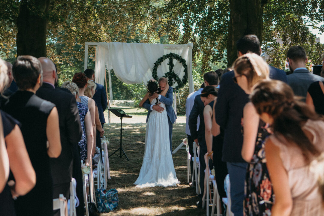 Brautpaar küsst sich unter Traubogen im Freien