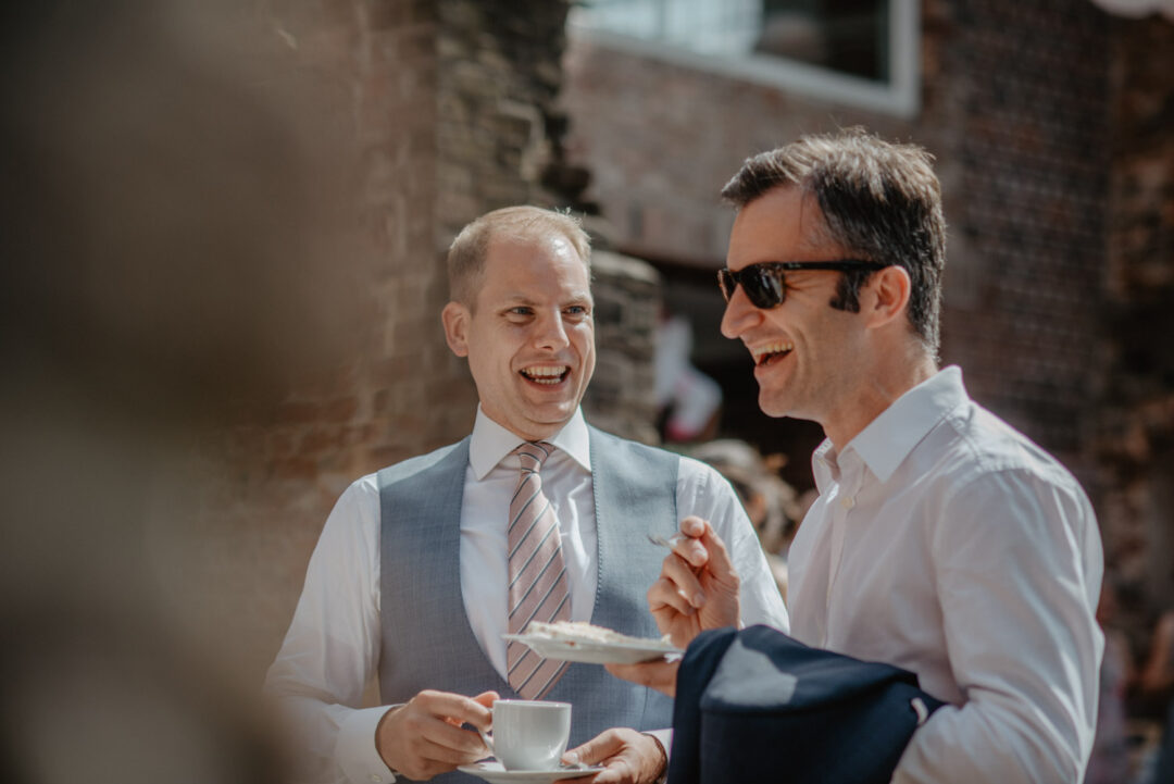 Bräutigam lacht mit Gast beim Kaffee nach der Trauung
