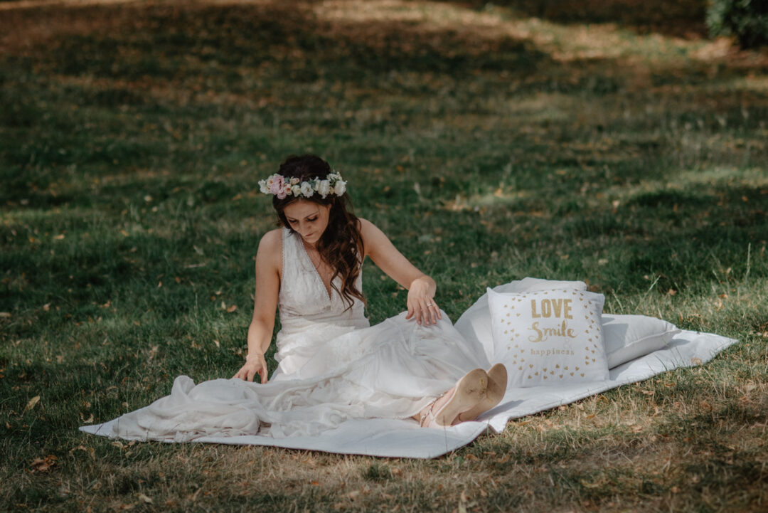 Braut sitzt entspannt auf Picknickdecke mit Kissen