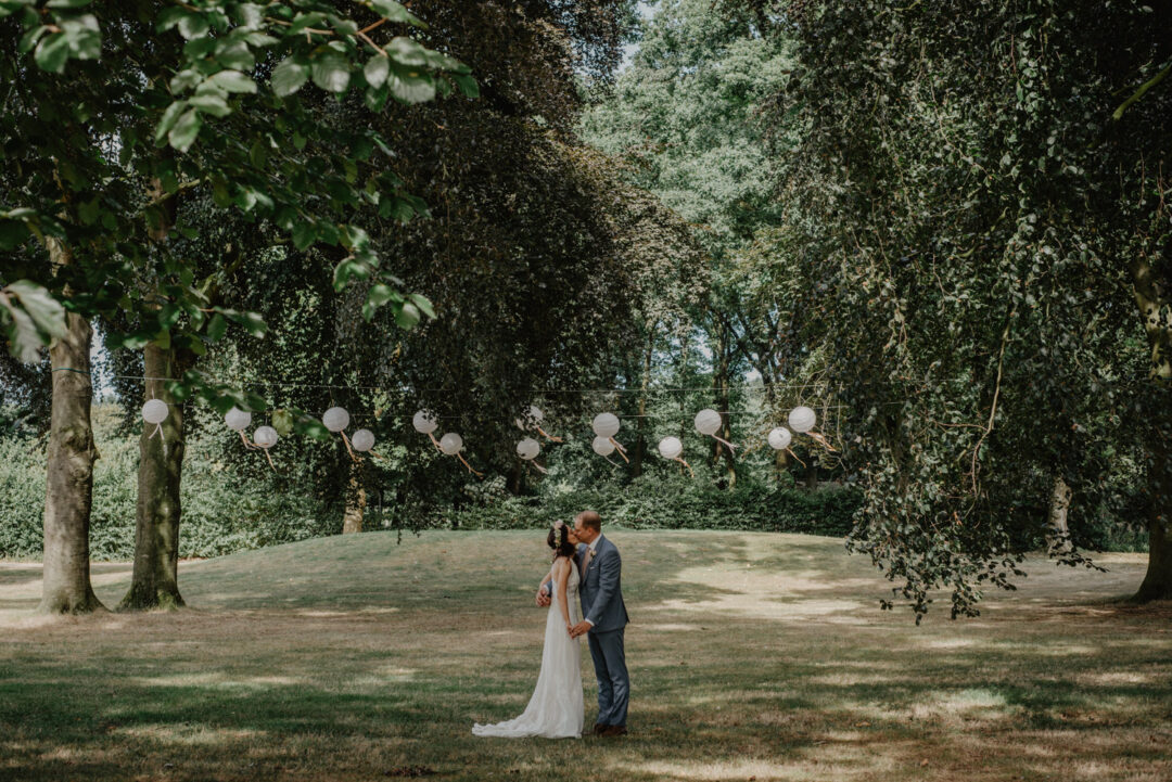 Brautpaar küsst sich unter weißen Lampions im Park