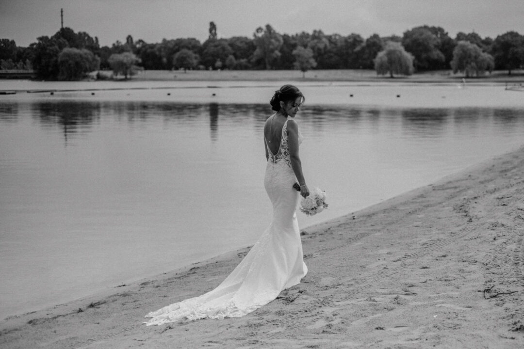 Braut geht barfuß am See entlang im Hochzeitskleid