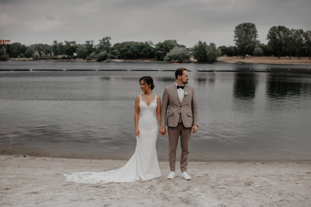 Braut und Bräutigam halten Händchen am Strand des Fühlinger Sees
