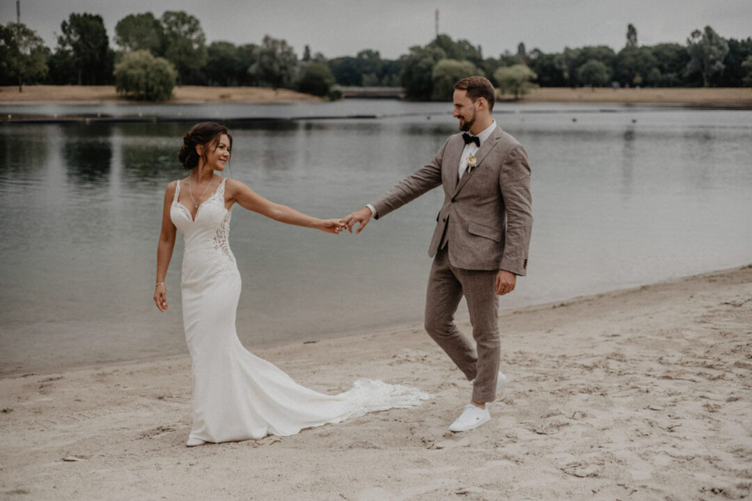 Hochzeitspaar spaziert am Sandstrand der freien Trauung am Fühlinger See