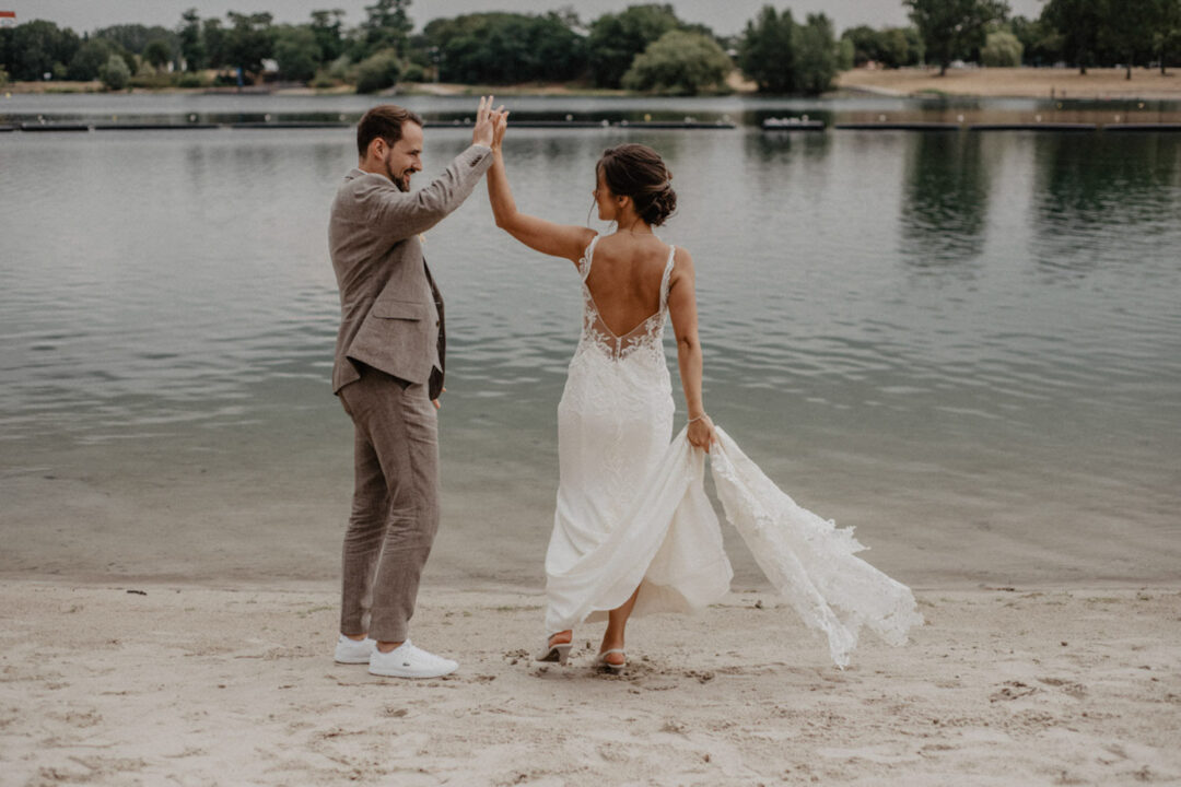 Braut und Bräutigam geben sich ein High Five am Wasser
