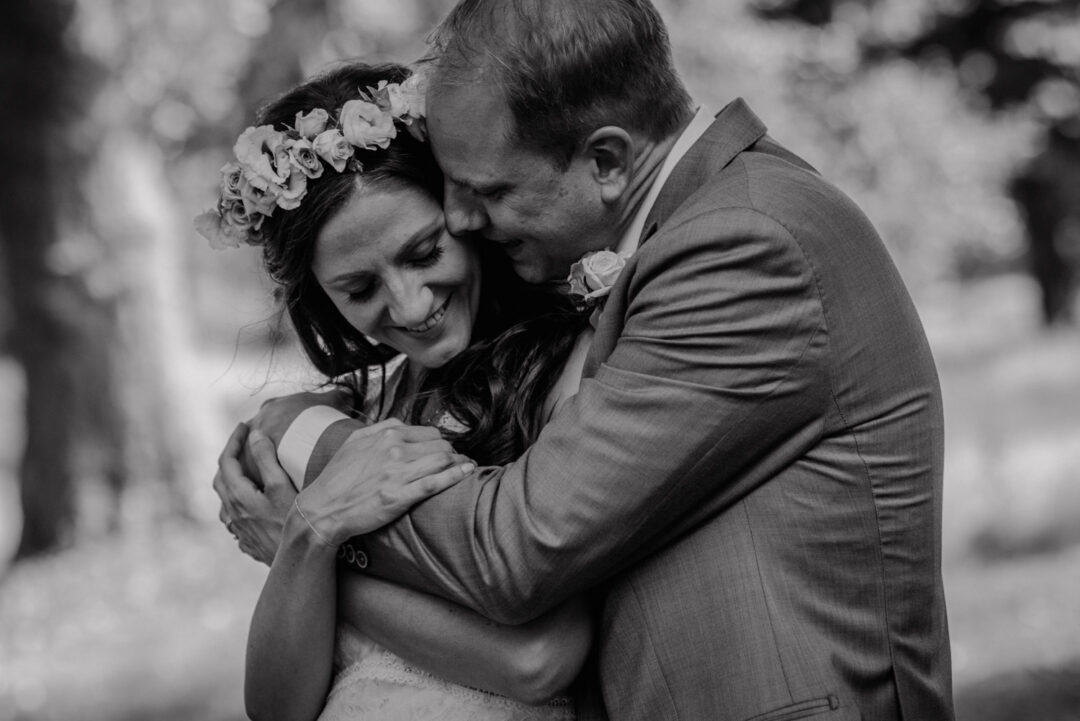 Bräutigam umarmt Braut liebevoll im Grünen