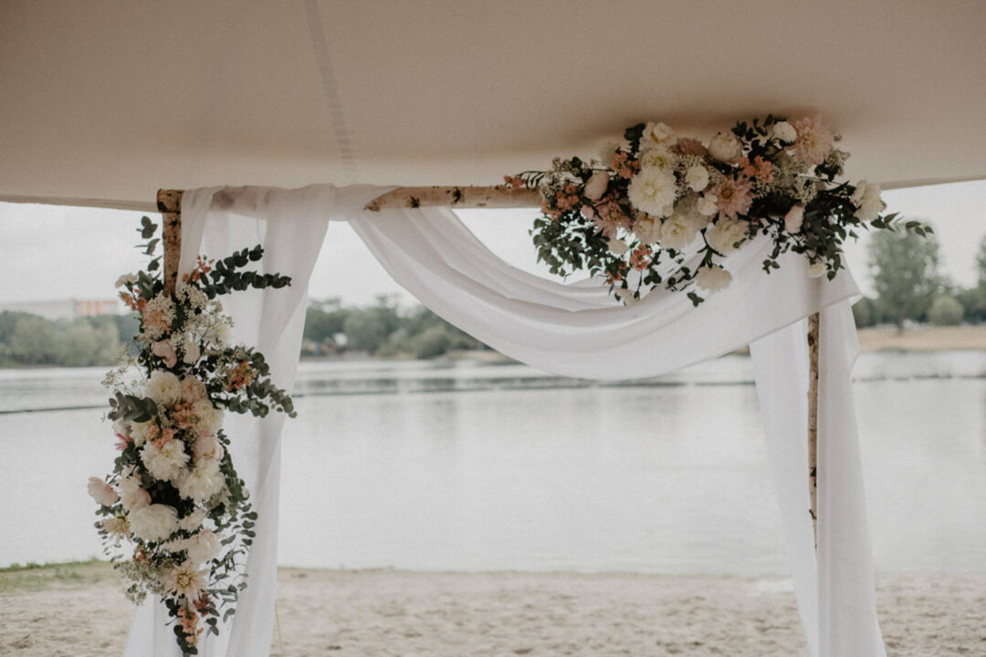 Floraler Traubogen mit weißen Stoffen am Strand des Fühlinger Sees