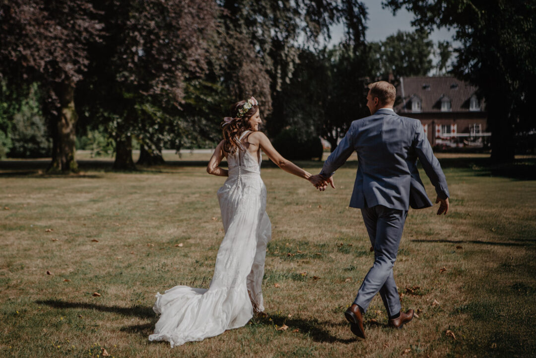 Brautpaar rennt Hand in Hand über die Wiese
